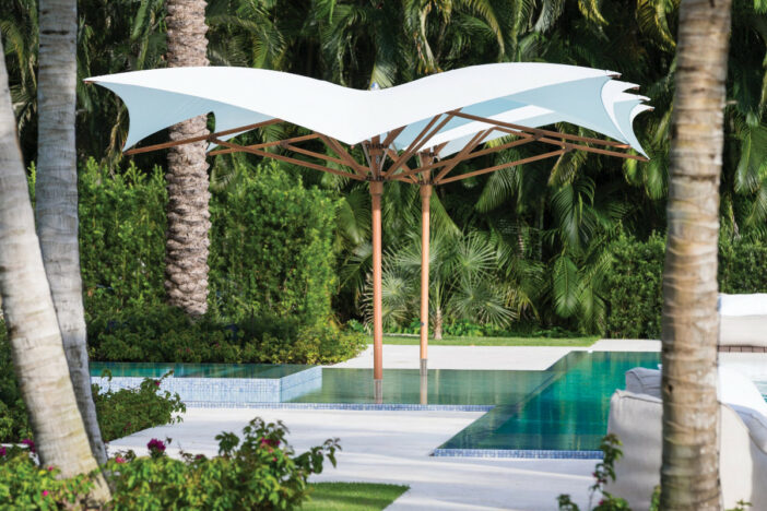 Two large TUUCI wooden center‑pole umbrellas with curved white canopies in a lush pool setting