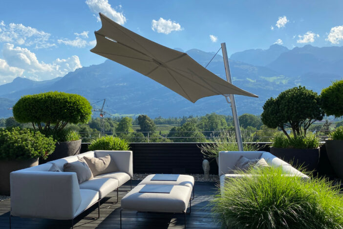 Umbrosa cantilever umbrella with angled silver post and flat off‑white canopy shading a lounge set in the mountains