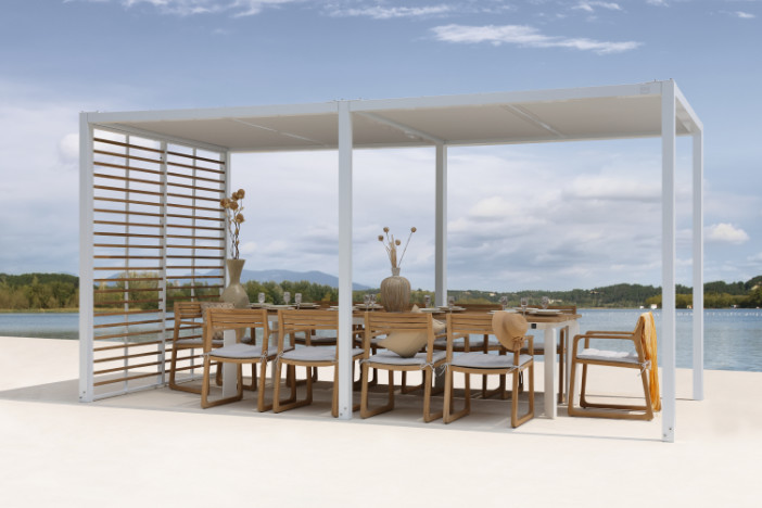Modern white aluminum frame canopy with sling roof and teak rod wall shading a rectangular dining set on a lakeside patio