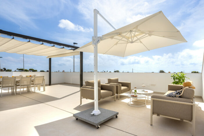 Black framed shade structure with off-white Roman shades over a dining set and a white cantilever umbrella shielding a lounge set
