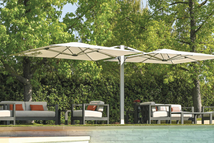 Silver cantilever umbrella with two off-white canopies shading lounge seating in a woody setting