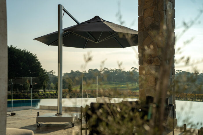 Modern silver cantilever umbrella and base with octagonal black canopy shading pool seating