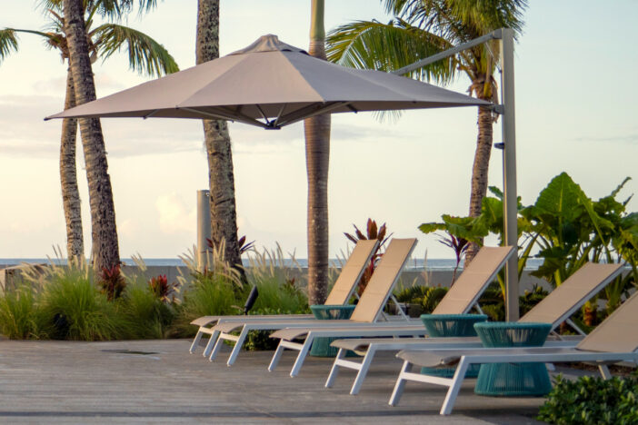 Modern cantilever umbrella with octagonal taupe canopy shading sun loungers on a tropical pool deck