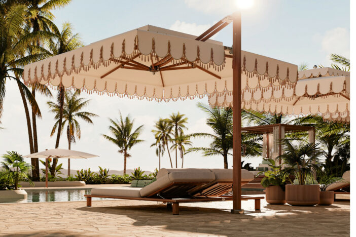 Large teak cantilever umbrellas with off-white square canopies with valances shading daybeds by a tropical pool