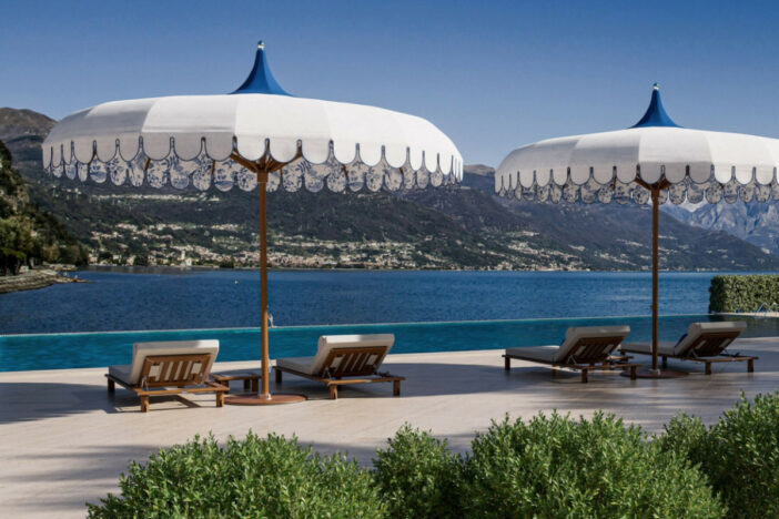 Decorative white and blue center pole umbrellas with valances between wooden loungers with a scenic view