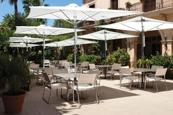 Metal center pole umbrellas with sleek square white canopies through dining tables in a courtyard restaurant