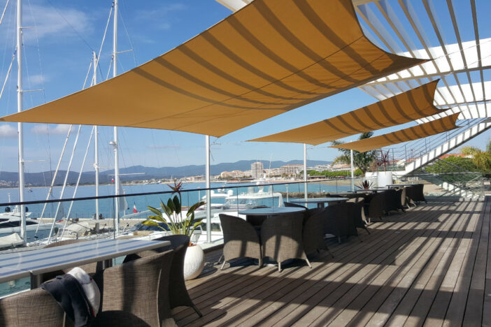 Off-white shade sails and a pergola awning stretch over marina restaurant deck