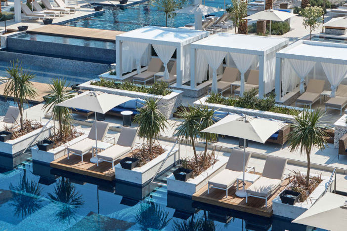 Spacious multi-level resort pool with white cabanas and center pole umbrellas shading loungers