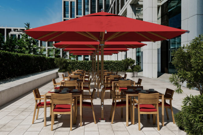 Large square red center-pole umbrellas shading teak dining sets on a spacious urban restaurant patio