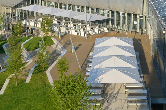 Large white rectangular center pole umbrellas shading benches and tables on a split-level corporate terrace
