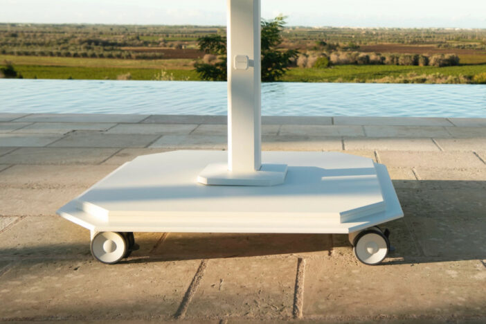 Streamlined white octagonal patio umbrella base wit wheels on a grey brick patio